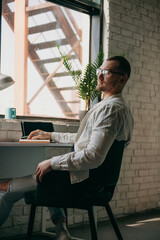 Thoughtful man holding pen and looking away while sitting at his working place in office. Using tablet.