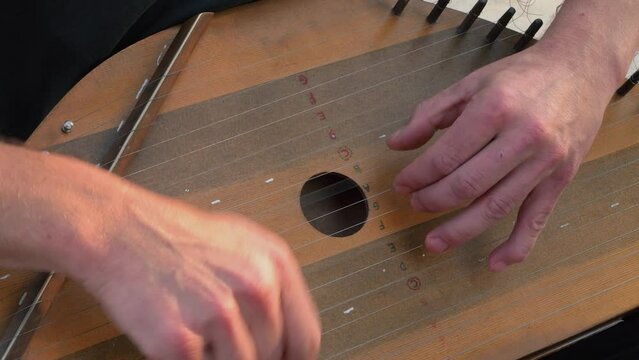 Musician hands beat the strings rhythmically. A man holds gusli on his lap and plays. Soft daylight. Close-up.