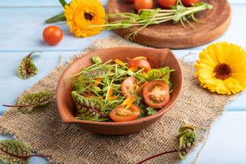 Vegetarian salad of tomatoes, marigold, microgreen on blue. Side view.