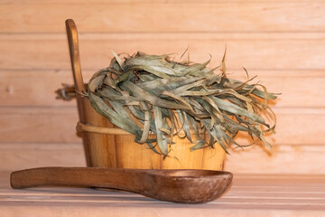 Close up photo of wooden spoon and bucket with linden broom in the sauna. Relaxing spa and body care.