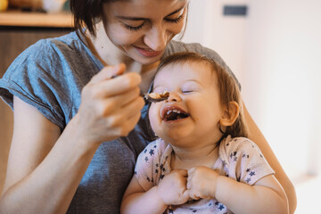 Baby feeding spoon by mother at home. Mom hand feeding baby. Family care. Baby care.