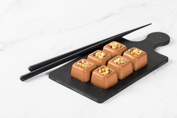 Mini Chocolate nut cream dessert in the shape of a square savarin on a serving board on a white background