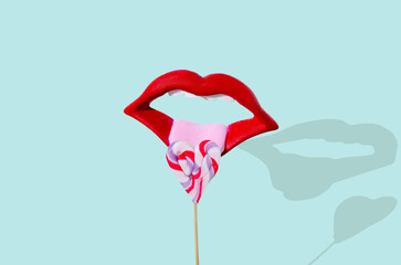 A wide open mouth with bright red lipstick and tongue licking a lollipop in a shape of a heart. Pastel green background. Surreal provocative design for Valentine's celebration card or banner.