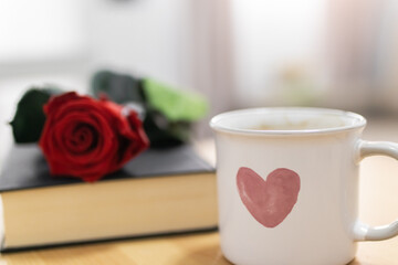 A cup of coffee with a drawn heart, a book and a rose