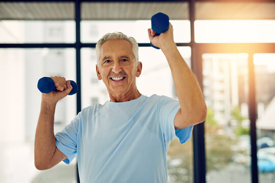 Staying active means aging well. Portrait of a fit senior smiling while lifting weights at the fitness center.