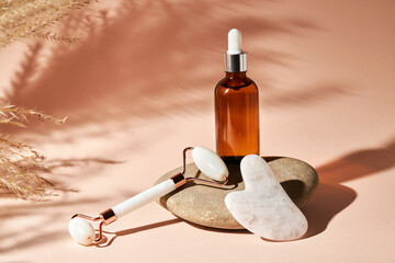 Gua Sha massage tools and essential oil on a river pebble stone  on a beige background. Home skin care anti-aging and beauty concept.