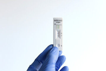 Unos dedos con guantes azules sujetando un test de antigenos covid-19 positivo sobre fondo blanco. 