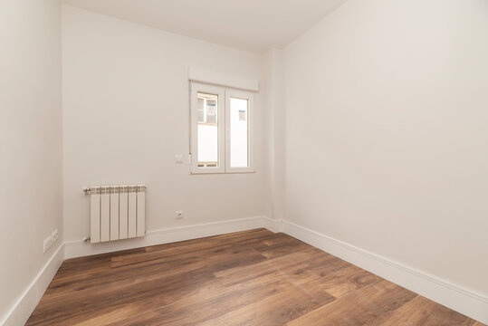 Empty residential building room with white painted aluminum radiator and dark parquet floor