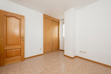 Empty room with built-in wardrobe with sliding wooden doors, stoneware floors and oak carpentry