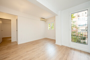 Empty living room with large window to one side, oak hardwood floors, air conditioning, and white painted walls