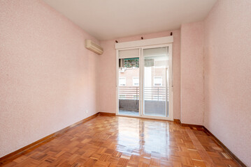 Living room with pink painted walls, reddish wooden floors and large window with white sliding doors leading out to a terrace