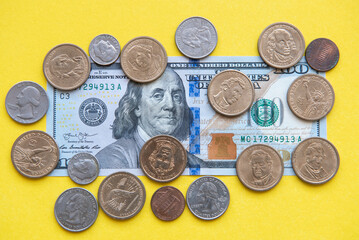 US dollar bills and coins. one hundred dollar bill and coins of different denominations around on a yellow background