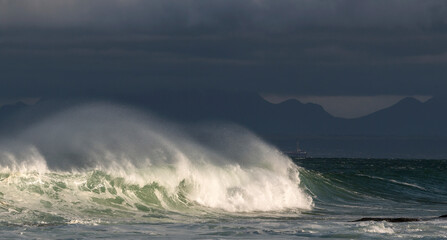 Seascape. Powerful ocean wave on the surface of the ocean. Wave breaks on a shallow bank. Stormy weather, stormy clouds sky background.