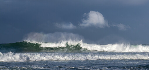 Seascape. Powerful ocean wave on the surface of the ocean. Wave breaks on a shallow bank. Stormy weather, stormy clouds sky background.