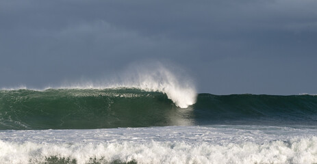 Seascape. Powerful ocean wave on the surface of the ocean. Wave breaks on a shallow bank. Stormy weather, stormy clouds sky background.