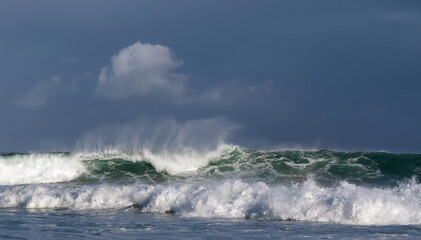 Seascape. Powerful ocean wave on the surface of the ocean. Wave breaks on a shallow bank. Stormy weather, stormy clouds sky background.