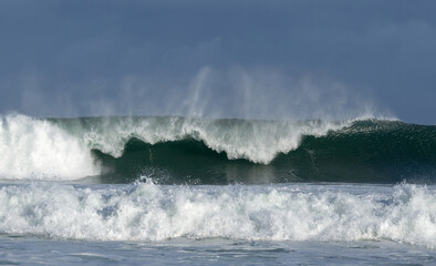 Seascape. Powerful ocean wave on the surface of the ocean. Wave breaks on a shallow bank. Stormy weather, stormy clouds sky background.