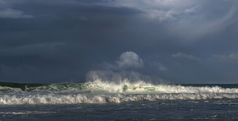 Seascape. Powerful ocean wave on the surface of the ocean. Wave breaks on a shallow bank. Stormy weather, stormy clouds sky background.