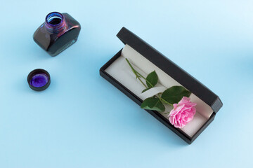 Vintage set of fountain pen, inkpot and blooming pink rose on blue background. Romantic minimal...