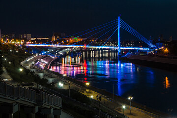 Beautiful view of the illuminated Embankment of Tura River and the Bridge of Lovers at dusk, Tyumen, Russia

