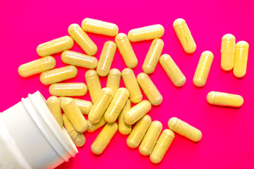 Bottle with spilled yellow pills on pink background, pharmacy concept