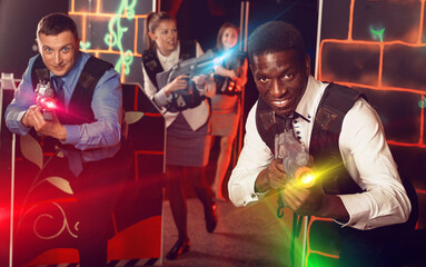 Satisfied positive men and women in business suits playing laser tag emotionally in dark room