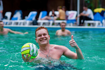 Young man posing with a ball in the pool/A cheerful happy young man playing ball in the pool