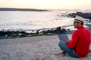 man sitting on the beach outdoor with a laptop alone doing telecommuting or remote work, back view