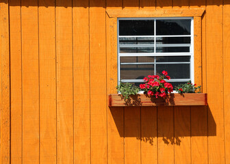 Small window with flower box is on  the bright orange wall of a house