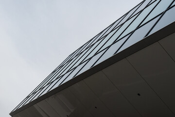 The exterior corner of a futuristic building with concrete panels, glass windows, and a grey sky....