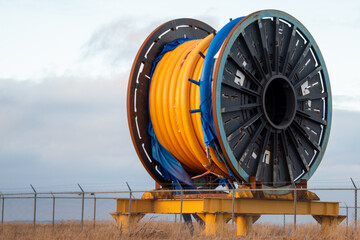 Bulk sub-sea industrial glass fiber optic cable on a metal spool on a ship's stand. The orange data...