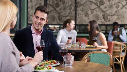 Cheerful handsome man with girlfriend enjoying evening meal at cozy restaurant