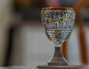 Traditional, decorative Jewish kiddush cup. Silver cup with saucer filled on a blurred background