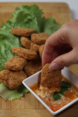 woman's hand holding a chicken nuggets at lunch, with ketchup and spicy buffalo sauce