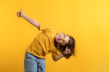 Determined Little Girl 8-10 Years Old in Basic Yellow T-shirt Eyeglasses on Daffodil Color Trend Wall Background Studio. Showing Ok Sign with Fingers. Happy Friendly Looking Child Pointing Thumbs Up