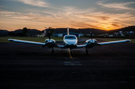 Avião bimotor de transporte aéreo de poucas pessoas, além do piloto. Avião estacionado ao crepúsculo vespertino. 