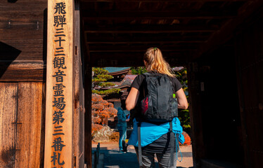 Blonde Female backpacker with jacket tied around her waste, entering temple in Japan