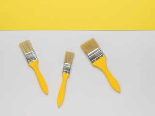 Three brushes with yellow wooden handles on a white and yellow background. Trending color.