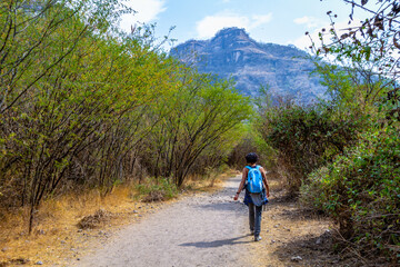 Fototapeta na wymiar A woman walks through an outdoors path in the nature towards a mountain in the horizon in Huentitan, Jalisco in Mexico