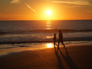 father and son stroll on beach at sunset