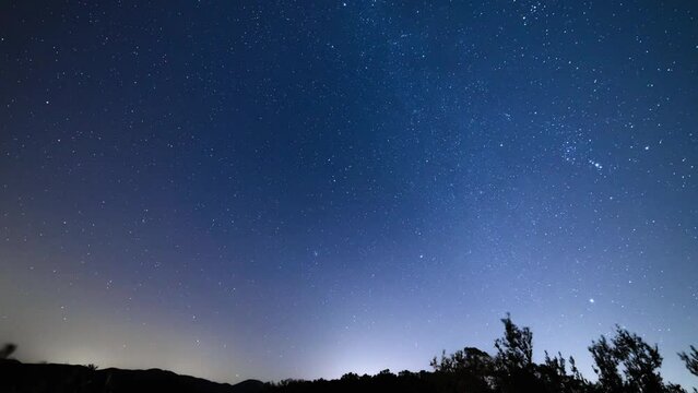 Night time lapse of stars and Milky Way moving behind the Tuscan hills. View of the blue sky  and starry night.