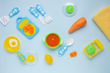 Carrot puree in a bowl and toy plastic utensils. Baby food concept. Top View