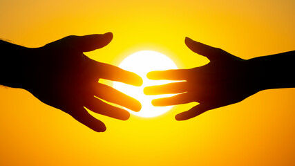 silhouette of male and female hands on the background of the setting sun. concept of communication and striving for closeness in society and family