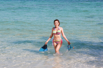 Young woman with bikini walking handle snorkel and fins on beach, summery holiday concept