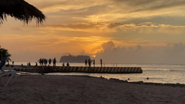 Silhouettes of people watching the sunset on Cozumel, Mexico. Big cruise ship swimming on the ocean during sunset. 