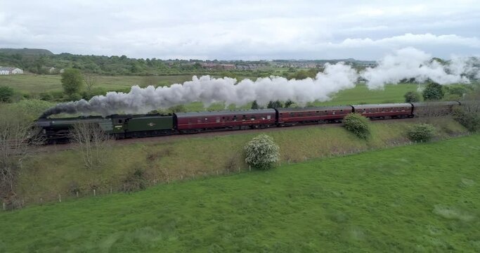 Low high to left tracking aerial shot of the Flying Scotsman steam train at full speed travelling through the countryside