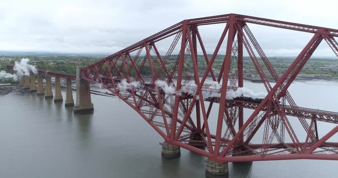Aerial pull back and track shot of the Flying Scotsman steam train crossing the first span of the Forth Rail Bridge