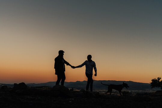 Silhouette of a gay couple in love holding hands while enjoying a walk on hills during the sunset. Love and relationships concept.