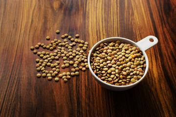 Taza medidora con lentejas sobre una mesa de madera. Granos de Lenteja.