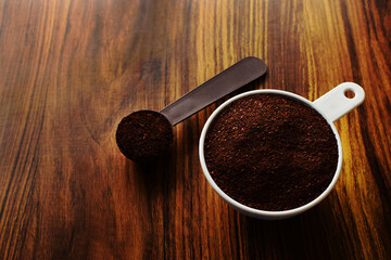 Taza medidora con café molido sobre una mesa de madera. Cuchara con café molido.